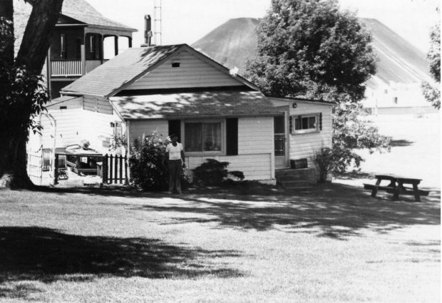Black and white photograph of a small cottage, a larger house behind it and large piles of coal in the background.