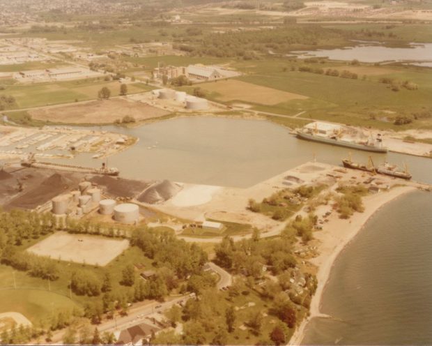 Colour aerial photograph of the land around the Oshawa Harbour before the Marina opened. There are three large ships docked in the port.