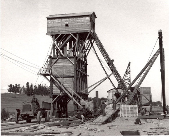 Black and white photograph of a tall wooden structure – a sand filter plant – with a staircase on the side and conveyor belts on the left side.