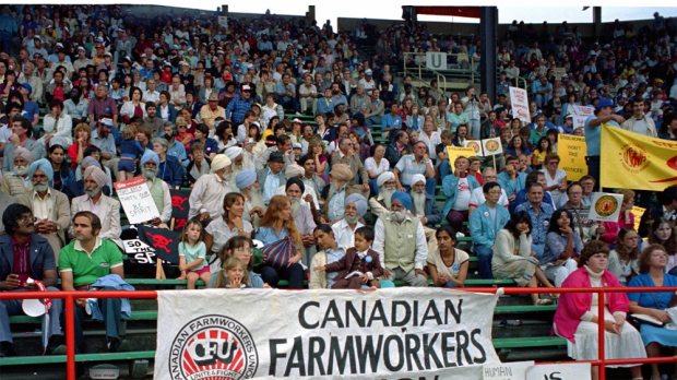 People and children seated on stadium seats hold banners and signs. The main banner reads Canadian Farmworkers Union.