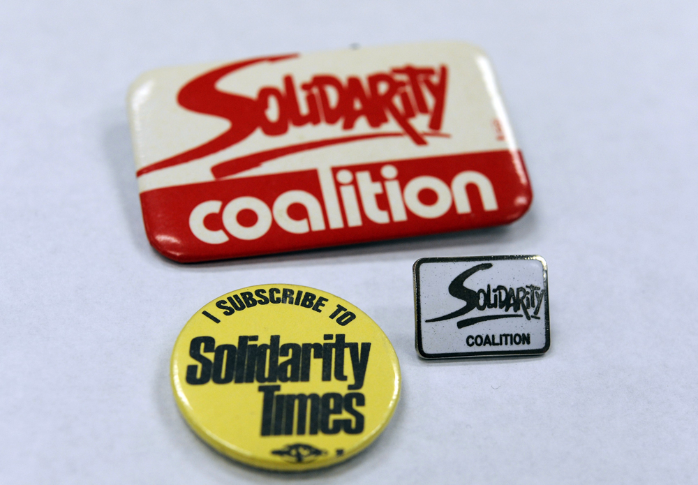 Three buttons are shown: “Solidarity Coalition” in red and white, “I subscribe to Solidarity Times” in yellow and black, and “Solidarity Coalition” enamel pin.