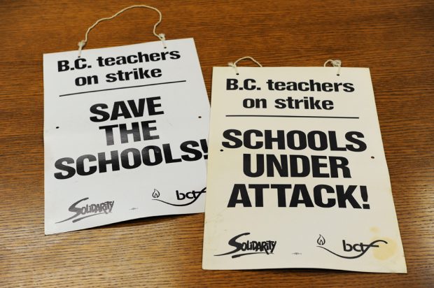 Two picket signs read: “BC teachers on strike, Save the Schools” and “BC teachers on strike, Schools Under Attack”.