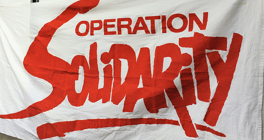 Un drapeau en tissu est affiché avec le logo d’Operation Solidarity d’imprimé sur fond blanc.