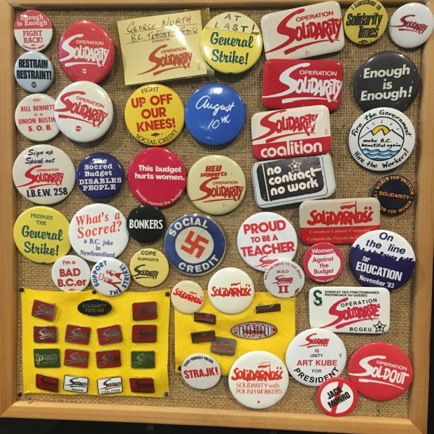A collection of pins and buttons from 1983 are grouped on a bulletin board.