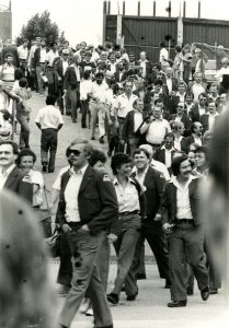 A parade of men and women are walking down a ramp. They are smiling and wearing uniforms.