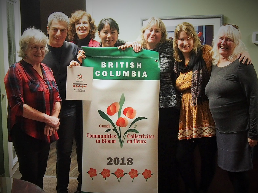 A group of seven people standing around a vinyl banner, with woman at centre holding it up. The banner reads: 