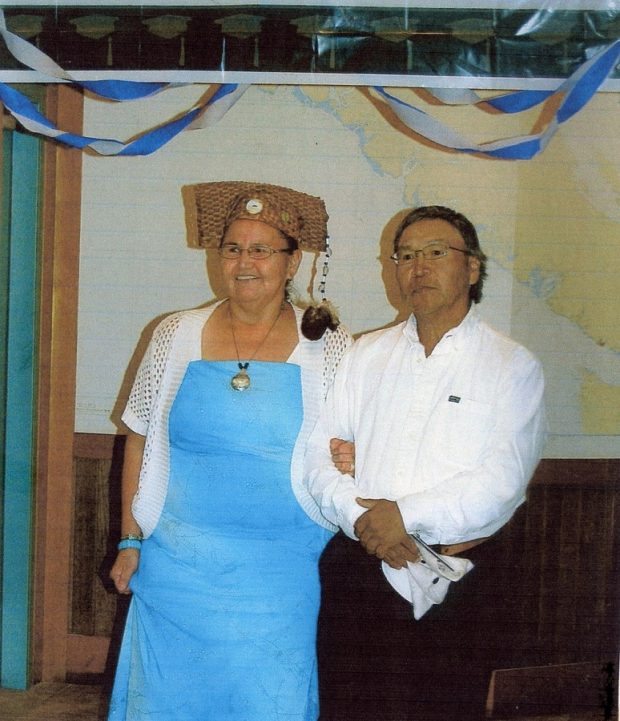A woman and a man arm in arm. The woman wears a traditional graduation cap made of woven bark and a fur tassle hangs from the top.