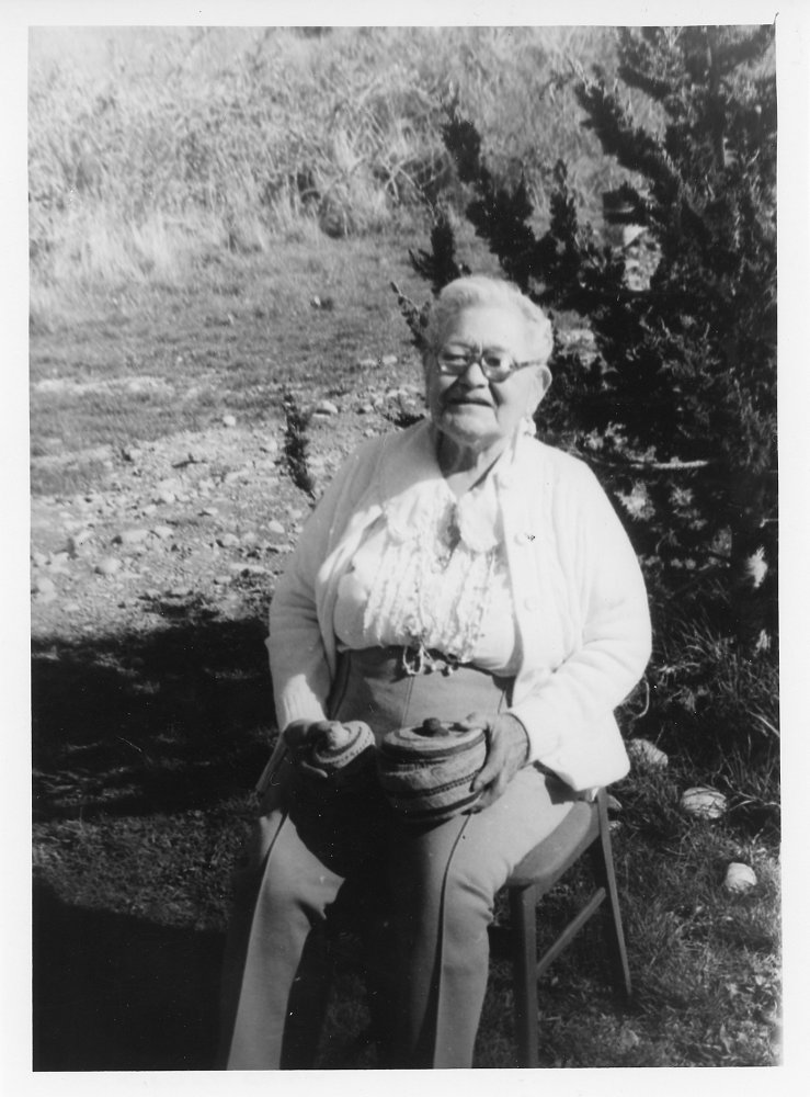 A woman sitting outdoors holding two woven baskets in her lap.