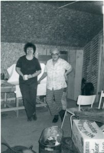 Photographie en noir et blanc de deux femmes debout dans un atelier ou dans un bureau.