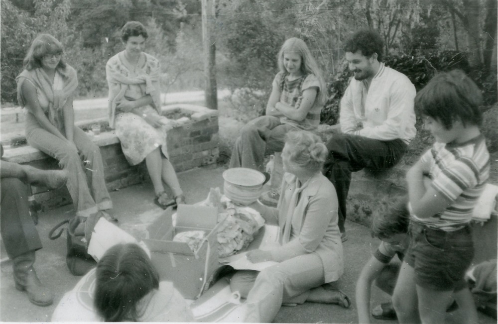 A group of students sitting outdoors on raised ledges around a woman at centre.