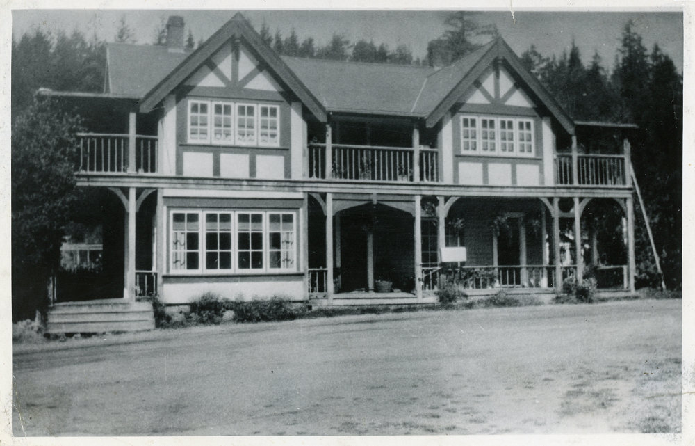 A black and white photograph of a two level building with a balcony and veranda.