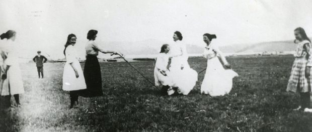 A black and white photograph of women skipping with a jump rope in a field.