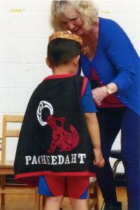 Woman adjusting cape of young boy. Cape features the words 