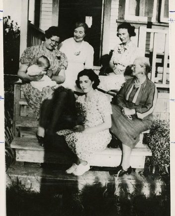 A black and white photograph of different generations of women from one family sitting on a porch together.