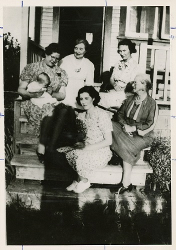 A black and white photograph of different generations of women from one family sitting on a porch together.
