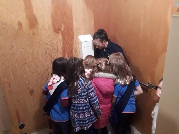 A woman doing a plumbing demonstration with small children gathered around her.