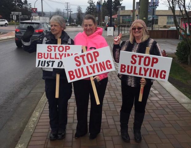 Three women on the sidewalk holding Stop Bullying signs.