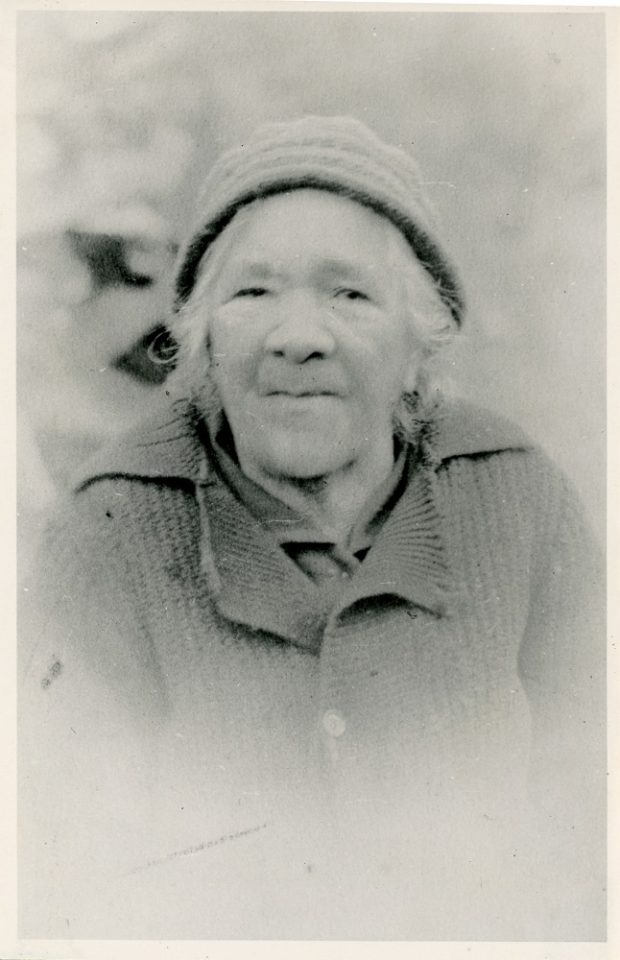 Black and white portrait photo of an elderly woman wearing a knitted hat and sweater.
