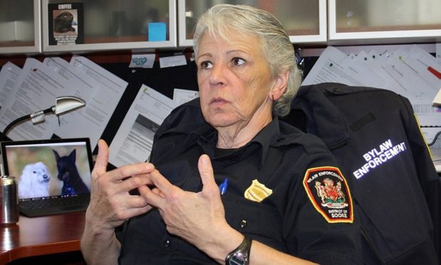In an office, a woman in a police uniform talks animatedly with her hands in front of her.