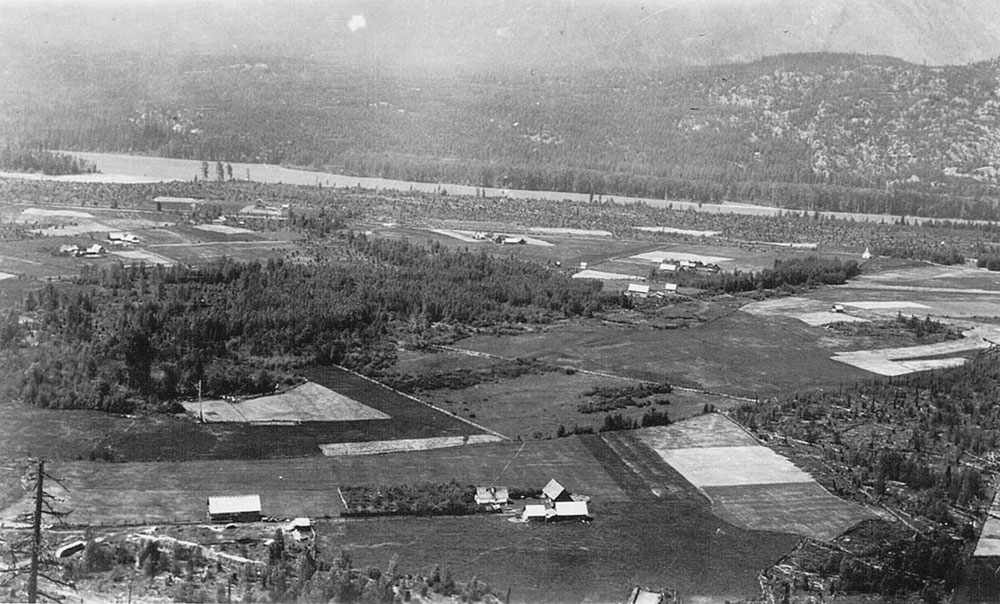 An aerial view black-and-white photograph showing farmland and the Mt. Cartier settlement. A river is visible in the background of the photo.