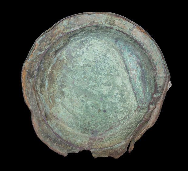 Greenish and rusty metal plate with some breakage at the base.