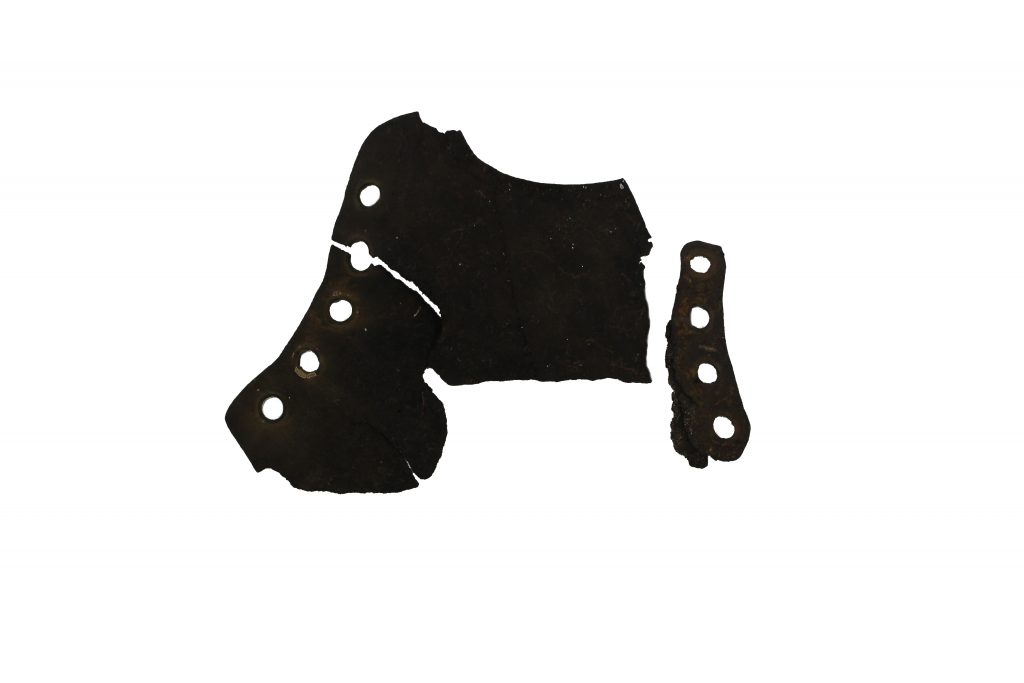 Black fragment of the top part of a shoe, lace up. 5 holes on large curved fragment and 4 holes on the smaller fragment.