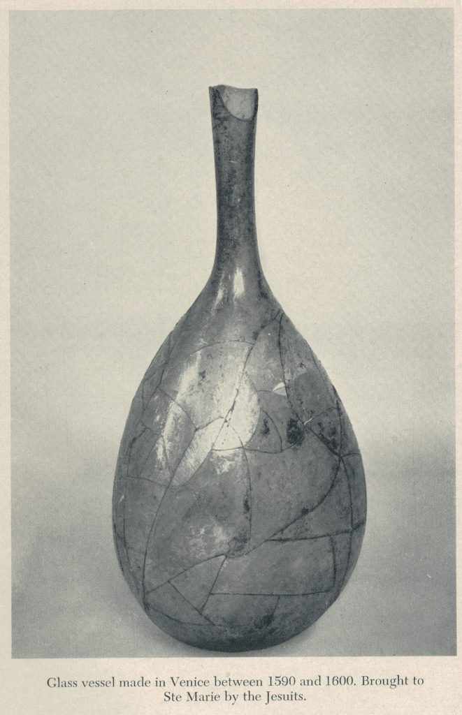 Sepia photograph of a complete glass container featuring a long narrow neck connecting to a wide body, slightly narrowing again at the base