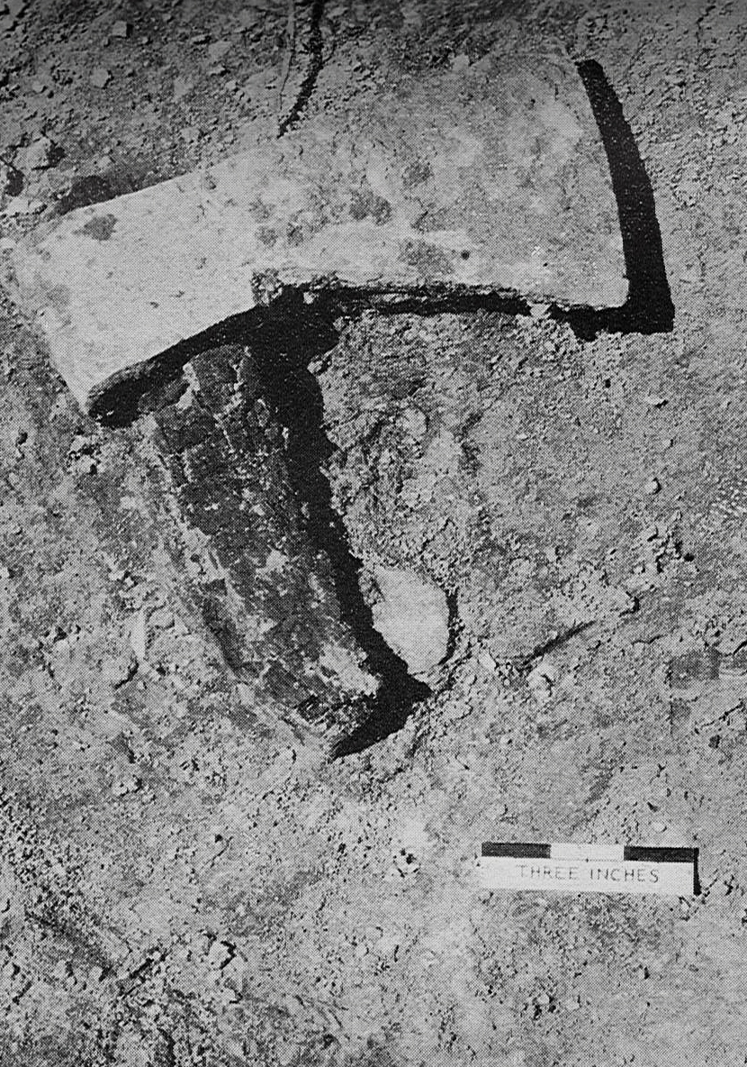 Grayscale photograph of iron axe with charred handle, before removal
