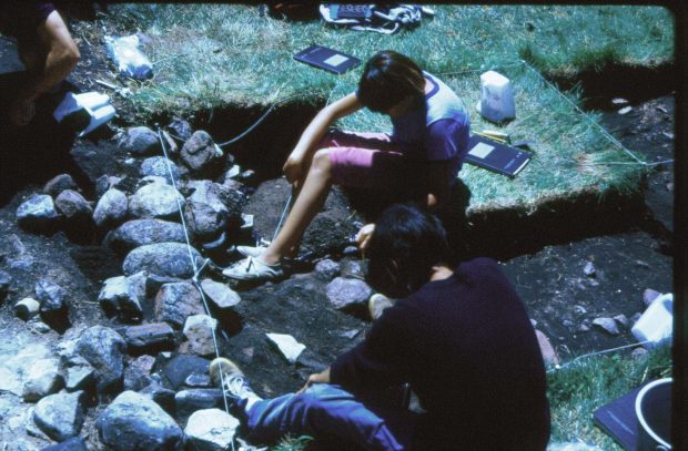 Image of two students excavating near the Fort walls. The topsoil has been removed in the area they are excavating and they are about 10cm below ground level.