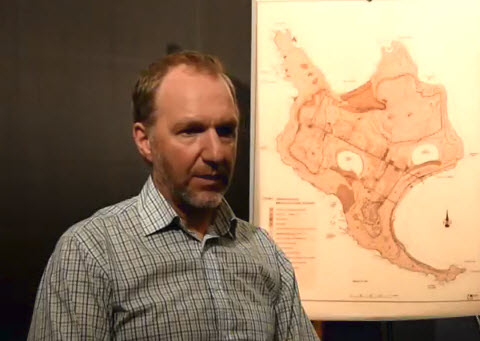 Image of Louis Lesage sitting to the left of a map of Christian Island.