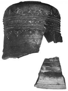 Photographie en noir et blanc du dessus et d’une partie de la base d’une cloche . Elle est entierement décorée de lignes et de motifs géométriques variés.