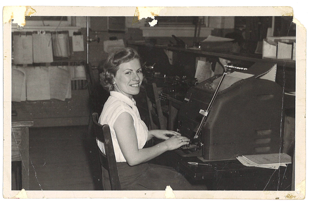 Black and white photo of a young girl sitting in front of a device with her hands on a typewriter-like keyboard.