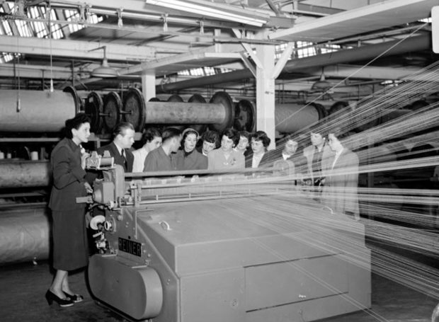 A group of young women gathered in front of a weaving machine inside the factory