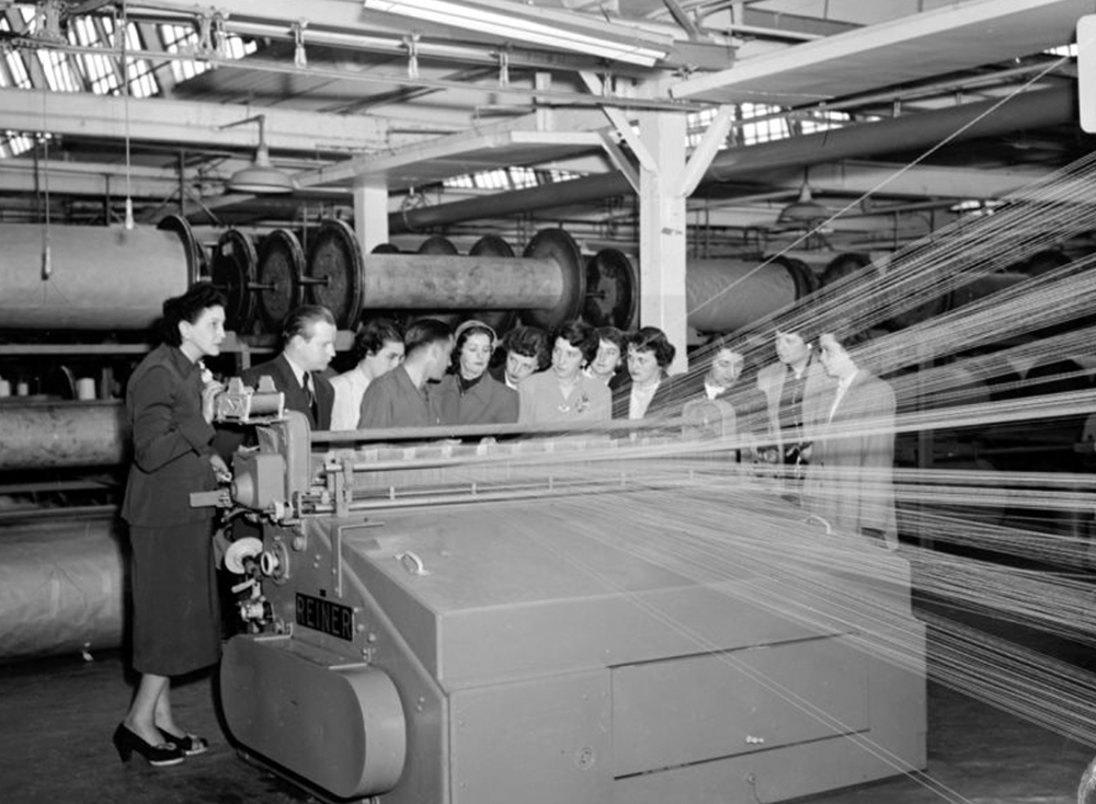A group of young women gathered in front of a weaving machine inside the factory