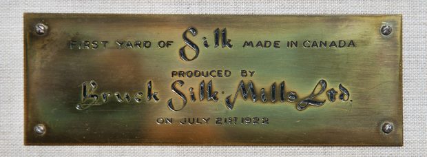 Commemorative brass plaque engraved with the inscription First Yard of silk made in Canada