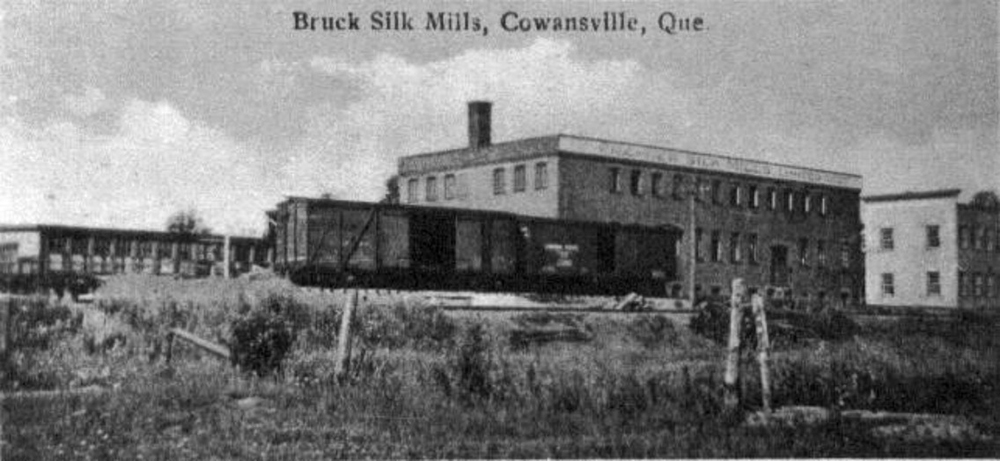 Black and white photo of the buildings of the Bruck Silk Mills around 1925 and, in the foreground, a railway and wagons.