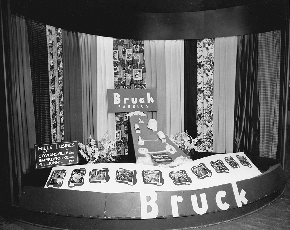 Trade show booth promoting Bruck Fabrics products from Cowansville, Sherbrooke and St-Johns with draperies, manufacturing tools and photos of the company's facilities on display.