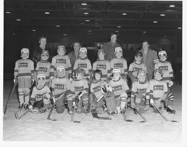 Bruck Silk Mills minor hockey team with coaches on an arena rink, photographed in three rows.