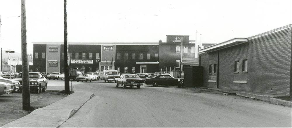 The entrance to the Bruck Silk Mills factory with 1970s automobiles parked in front.