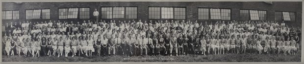 The employees and managers of the company pose in front of the factory on four rows.