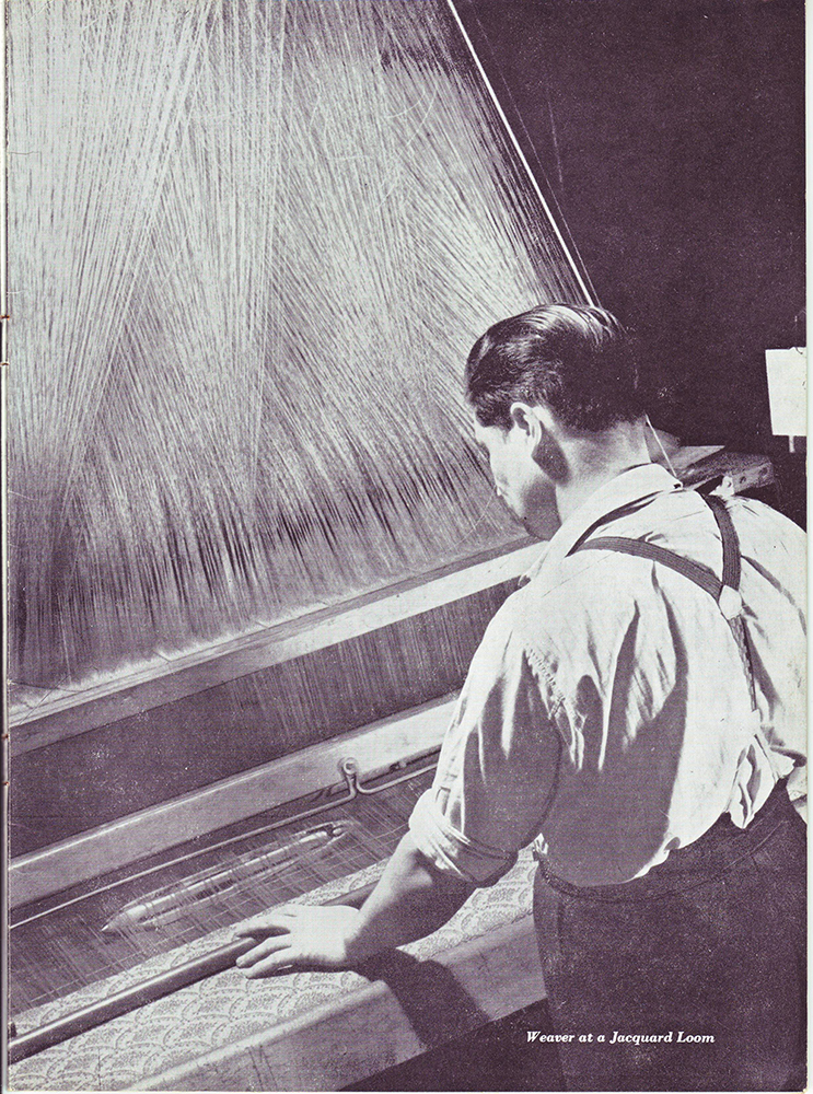 Black and white photo of a man seen from behind in front of a loom