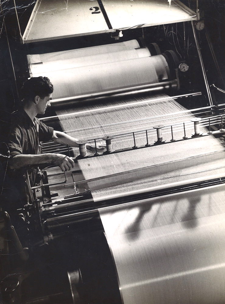 Black and white photo of a worker bent over a loom