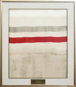 Frame displaying a piece of fabric with a red and gray stripe and a plaque identifying it as the first yard of woven silk in Canada.