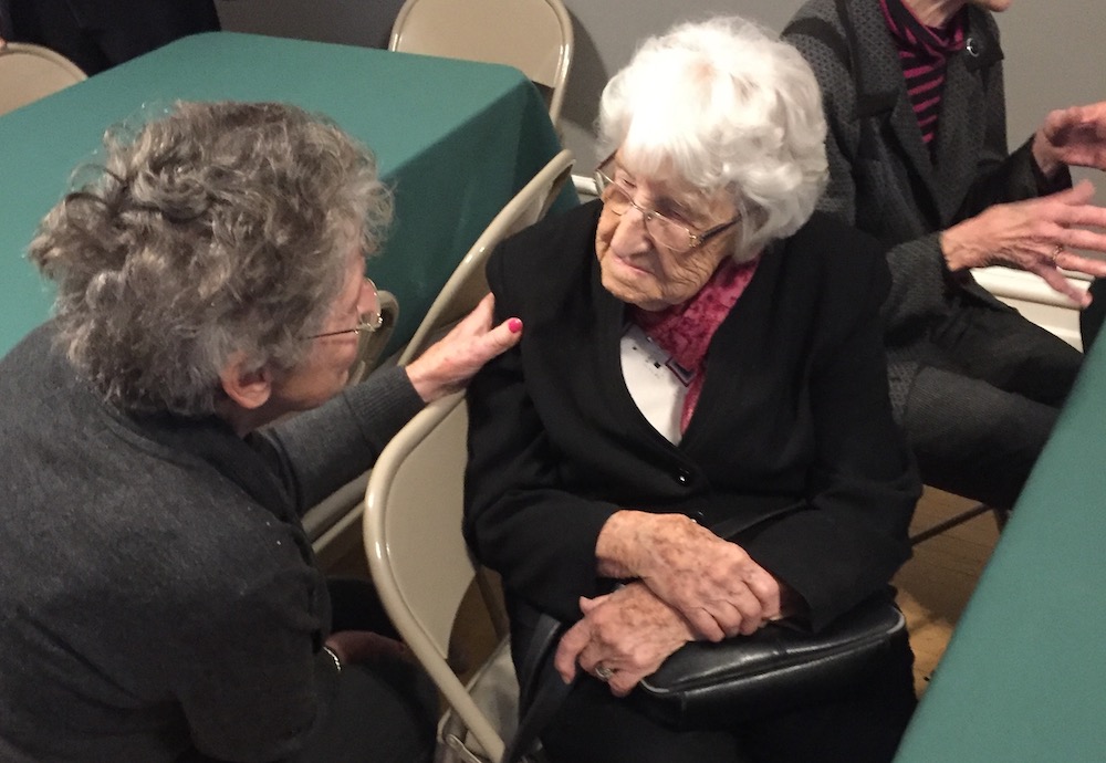 Two elderly women sitting at a table are talking to each other.