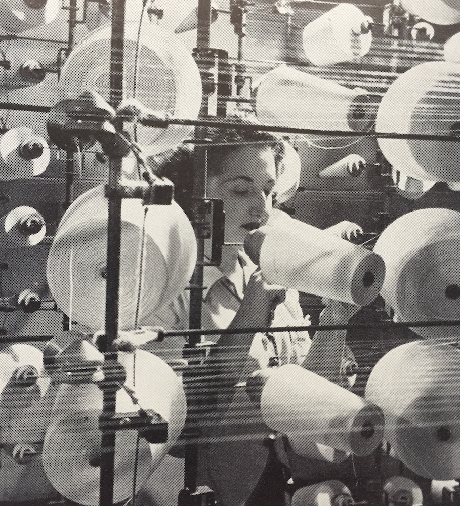 Black and white photo with a worker behind multiple spools of thread.