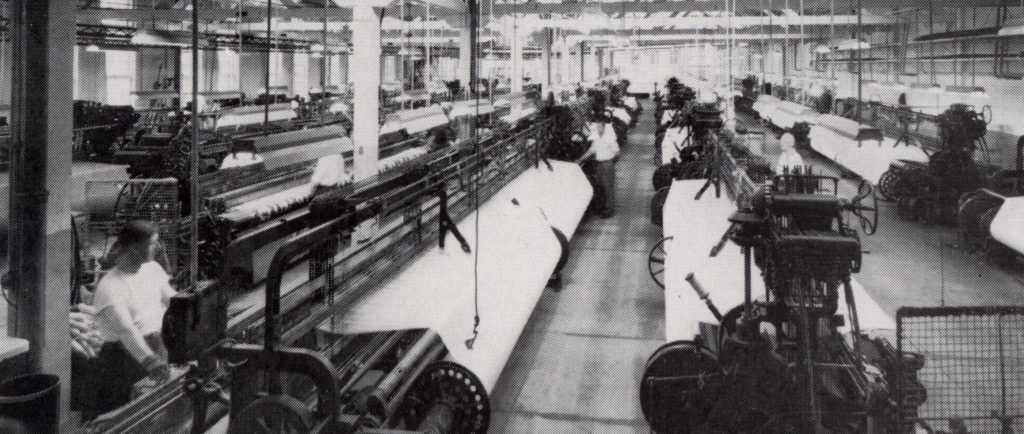 A factory floor with several rows of weaving machines.