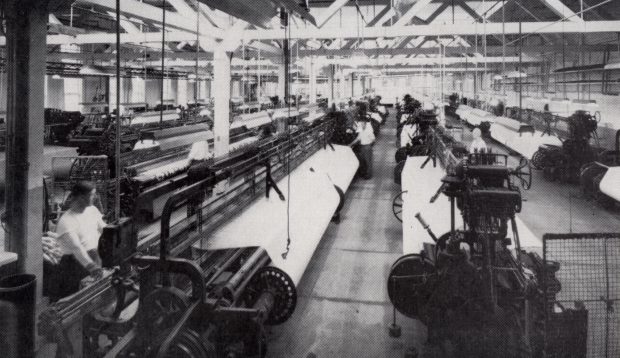 A factory floor with several rows of weaving machines.