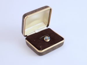 A gold and blue pin in a brown box.