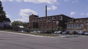 Picture of a brick factory with a parking lot in front.