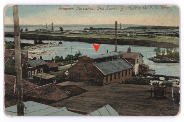 A postcard with a series of wood and brick houses in the foreground and a lumber mill in the background, separated by a river.